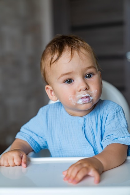 Criança engraçada suja come mingau na cadeira Comida infantil