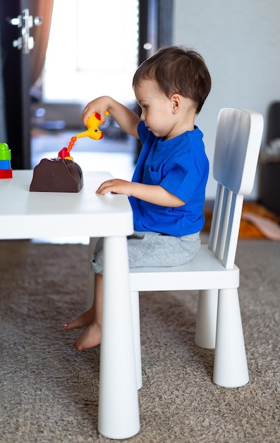 Criança entretida em uma brincadeira em uma mesa com um brinquedo Um garotinho sentado em uma mesa brincando com um brinquedo