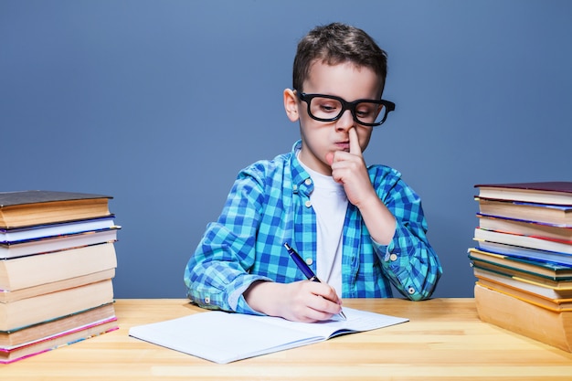Criança escrevendo no caderno e pega seu nariz, o conceito de lição de casa da escola. Jovem aluno na mesa da sala de aula