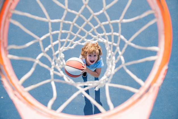 Criança espantada a jogar basquete, segurando uma bola com uma cara feliz.