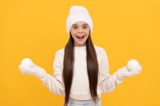 Criança espantada com chapéu de inverno e luvas seguram bolas de neve no natal de fundo amarelo