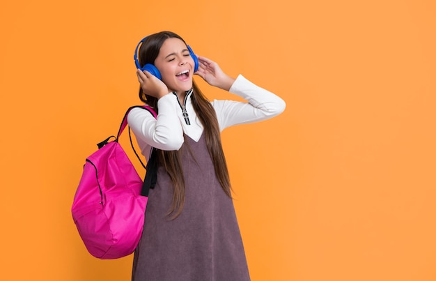 Criança espantada em fones de ouvido com mochila escolar em fundo amarelo