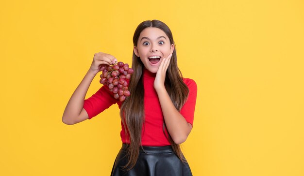 Criança espantada feliz segura cacho de uvas em fundo amarelo
