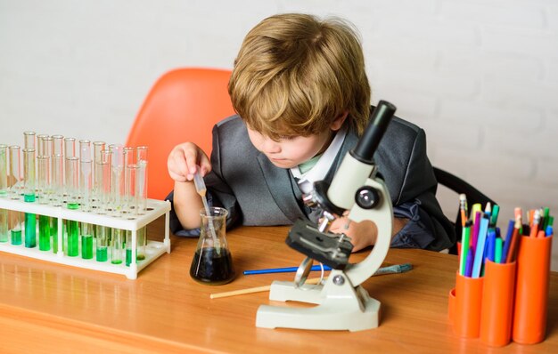 Criança estuda química lição escolar educação escolar criança gênio bebê análise química conceito de ciência criança superdotada e prodígio menino usa microscópio e tubos de ensaio na sala de aula da escola