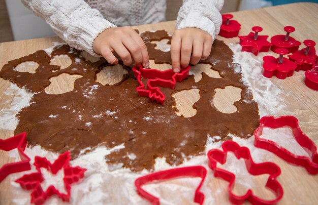 Criança faz biscoitos de Natal de massa de pão de gengibre e cortadores de biscoito. Conceito de cartão de Natal.