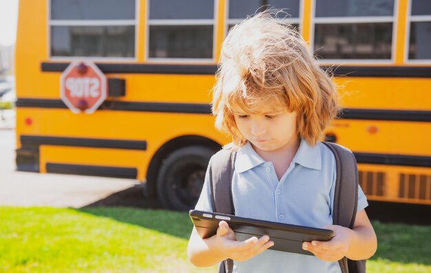 Criança faz lição de casa com tablet no parque perto de ônibus escolar criança ao ar livre