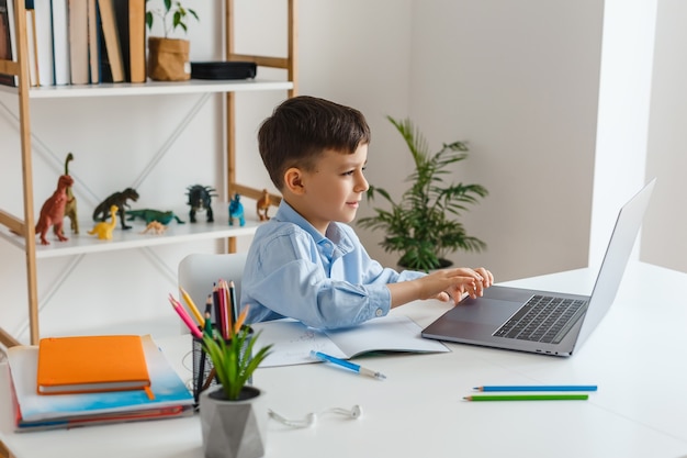 Criança fazendo lição de casa usando laptop Escola primária de elearning Menino estudando online em casa