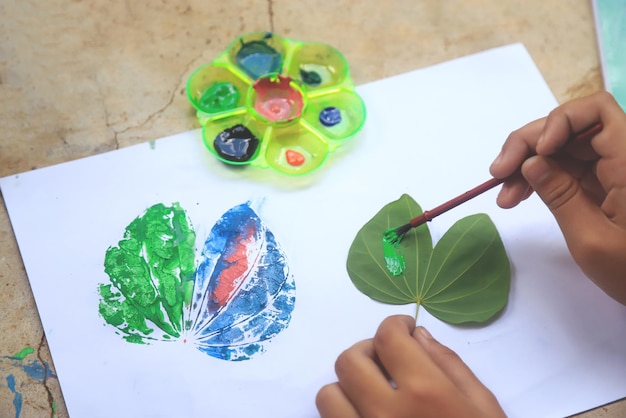 Criança fazendo trabalho de arte com aquarela para fazer padrão da natureza por folha de árvore