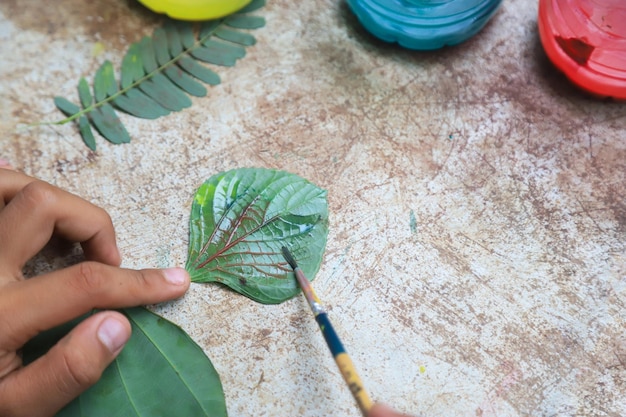 Foto criança fazendo trabalho de arte com aquarela para fazer padrão da natureza por folha de árvore