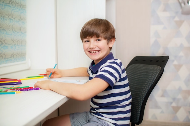 Criança feliz 7-8 anos de idade se senta em uma mesa e desenha