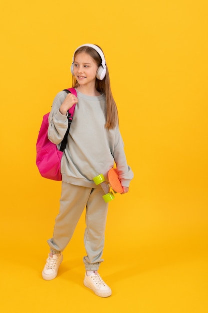 Criança feliz adolescente com mochila escolar e penny skate ouve música em fones de ouvido, tempo de escola.