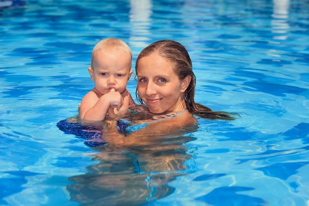 Criança feliz aprende a nadar com a jovem mãe na piscina.