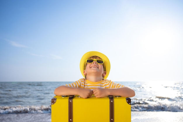 Criança feliz aproveitando o sol contra o fundo do céu azul Criança com mala se divertindo na praia Férias de verão e conceito de férias