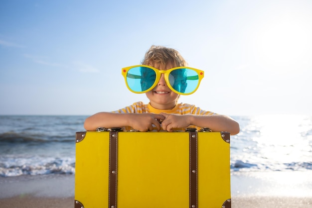 Criança feliz aproveitando o sol contra o fundo do céu azul Criança com mala se divertindo na praia Férias de verão e conceito de férias