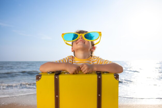 Criança feliz aproveitando o sol contra o fundo do céu azul Criança com mala se divertindo na praia Férias de verão e conceito de férias