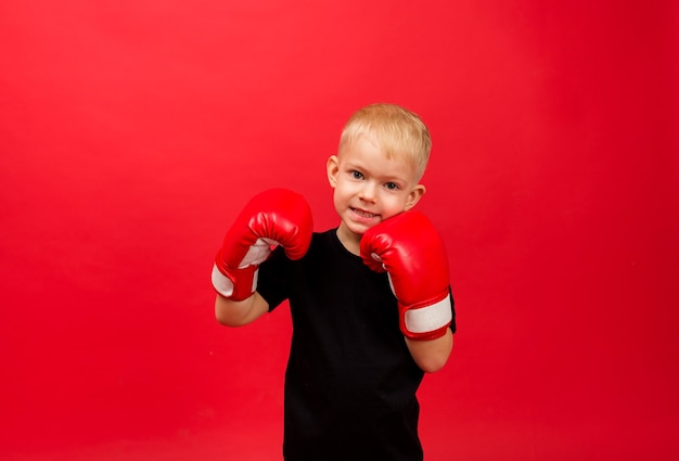 Criança feliz boxer menino com luvas de boxe vermelhas na parede vermelha