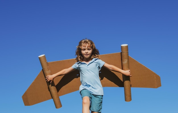 Criança feliz brincando com asas de brinquedo contra o fundo do céu de verão Líder de sucesso infantil e conceito de vencedor