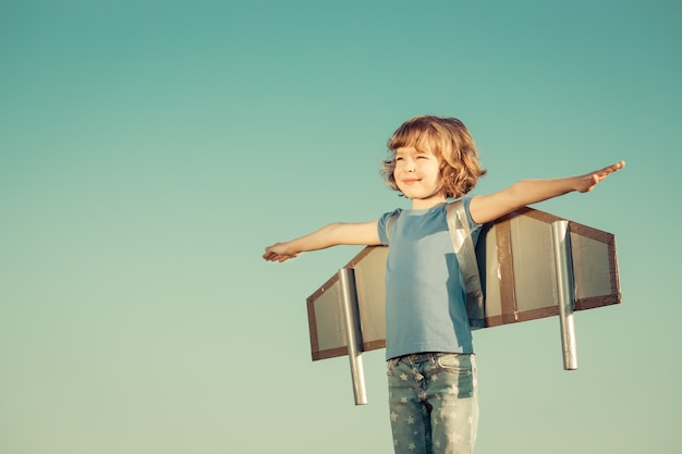 Criança feliz brincando com asas de brinquedo contra o fundo do céu de verão. Retro tonificado