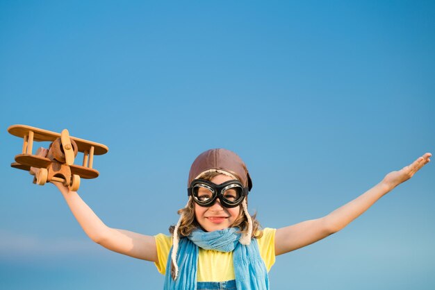 Foto criança feliz brincando com avião de brinquedo ao ar livre criança se divertindo contra o fundo do céu de verão conceito de viagem e imaginação