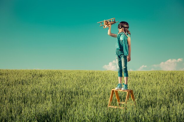 Criança feliz brincando com avião de brinquedo ao ar livre no campo de verão Conceito de viagem e férias Imaginação e liberdade