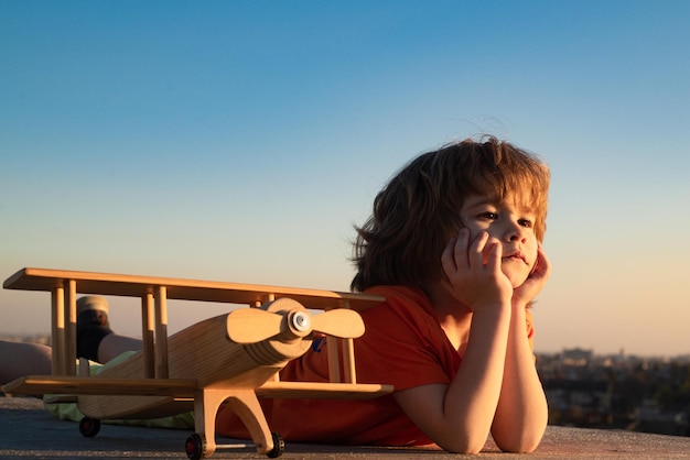 Criança feliz brincando com avião de brinquedo contra o fundo do céu azul criança bonita de 8 anos em um dia ensolarado de verão crianças sonham em viajar