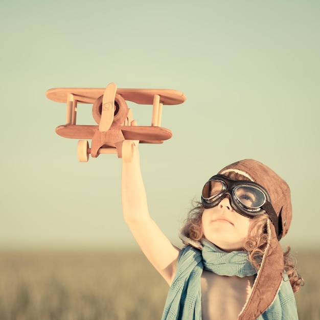 Foto criança feliz brincando com avião de brinquedo contra o fundo do céu azul de verão