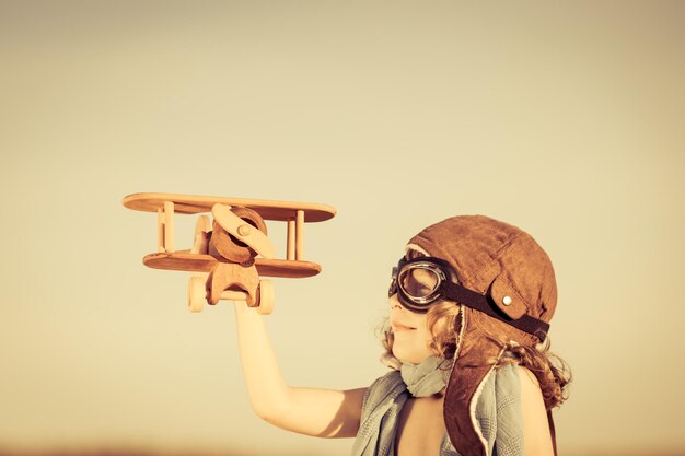 Criança feliz brincando com avião de brinquedo contra o fundo do céu azul de verão