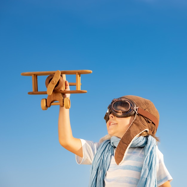 Criança feliz brincando com avião de madeira vintage. Garoto se divertindo ao ar livre no verão. Conceito de imaginação e liberdade