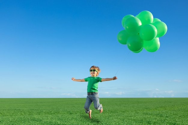 Criança feliz brincando com balões multicoloridos brilhantes ao ar livre Criança se divertindo no campo verde primavera contra o fundo do céu azul Conceito de estilo de vida saudável e ativo