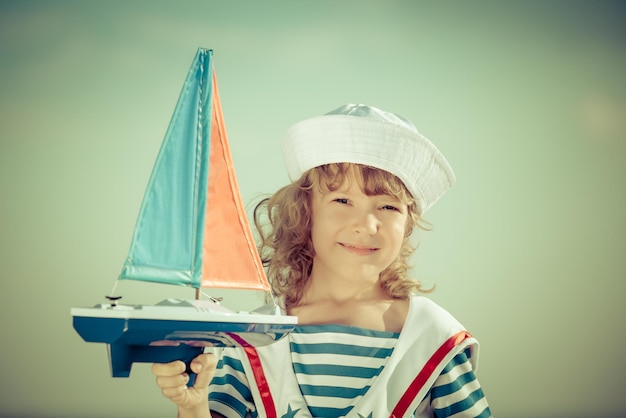 Criança feliz brincando com barco à vela de brinquedo contra o fundo do céu azul