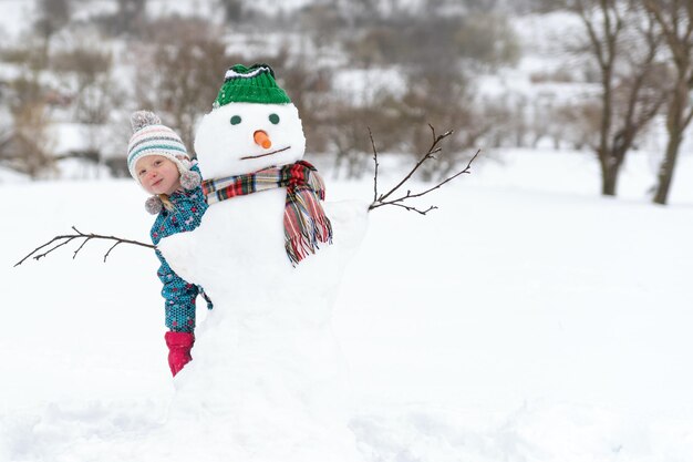 Criança feliz brincando com boneco de neve em uma caminhada de inverno Criança fora de construção de figura de neve Atividades de inverno para crianças