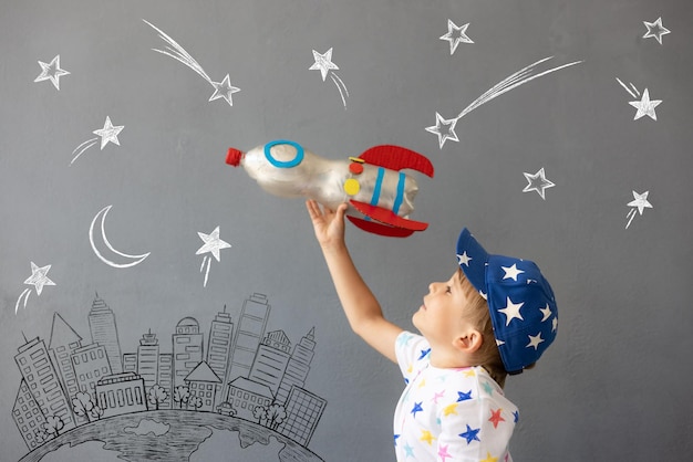 Foto criança feliz brincando com foguete de brinquedo contra o fundo da parede de concreto garoto finge ser astronauta imaginação e conceito de sonho de crianças