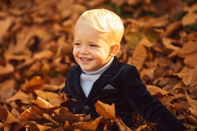 Criança feliz brincando com folhas caídas no parque de outono garotinho se divertir brincando com folhas caídas de ouro.