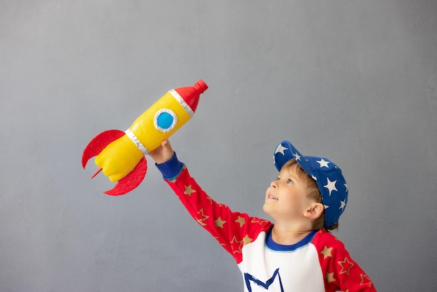 Criança feliz brincando com um foguete de brinquedo contra o fundo da parede de concreto