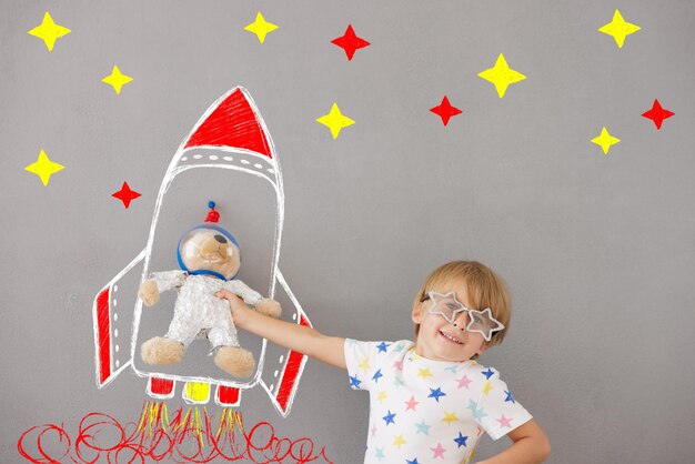 Criança feliz brincando com ursinho de pelúcia em casa. Garoto finge ser astronauta. Imaginação e conceito de sonho de crianças