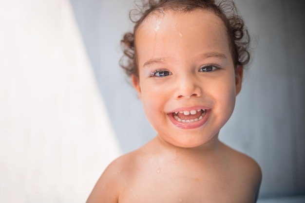 Criança feliz brincando em uma piscina inflável no quintal criança encaracolada sorrindo e brincando com água