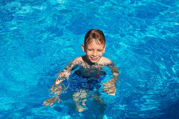 Criança feliz brincando na água azul da piscina em um resort tropical à beira-mar.