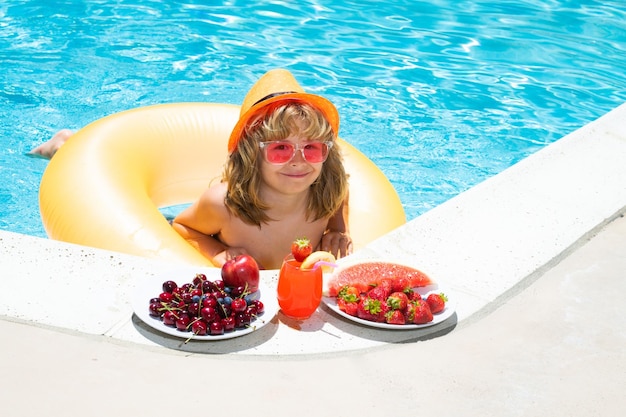 Criança feliz brincando na piscina Férias de verão para crianças Fruta de verão para crianças Garotinho relaxando em uma piscina se divertindo durante as férias de verão