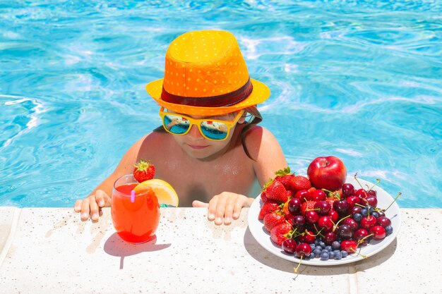 Criança feliz brincando na piscina Férias de verão para crianças Fruta de verão para crianças Garotinho relaxando em uma piscina se divertindo durante as férias de verão