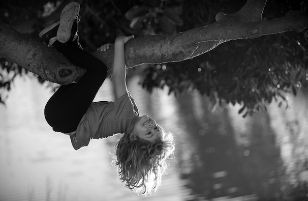 Foto criança feliz brincando no jardim subindo na árvore de cabeça para baixo conceito de infância