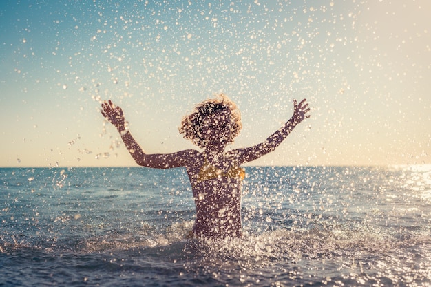 Foto criança feliz brincando no mar. garoto se divertindo nas férias de verão. conceito de estilo de vida ativo e saudável