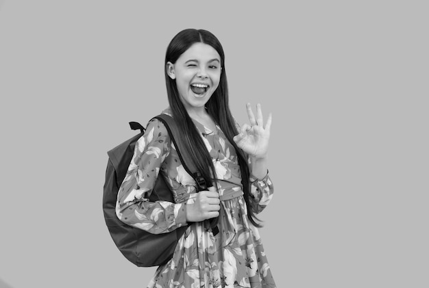 Criança feliz carrega mochila indo para a escola piscando e mostra o gesto ok de volta à escola