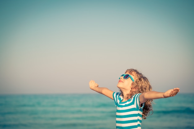 criança feliz com as mãos abertas contra o azul do mar e do céu