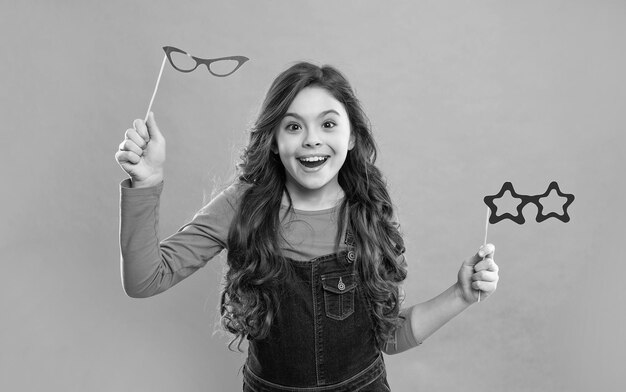 Criança feliz com cabelo encaracolado segura acessório de festa de óculos divertidos