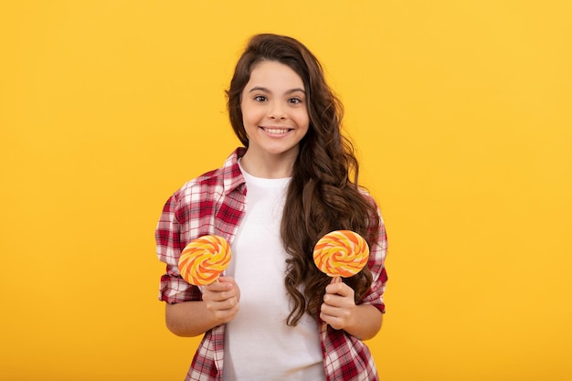 Criança feliz com cabelo longo cacheado em camisa quadriculada segurar pirulito doce de caramelo em fundo amarelo, gostoso.