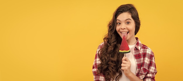 Criança feliz com cabelo longo encaracolado lamber pirulito doce de caramelo na infância de fundo amarelo Criança adolescente com espaço de cópia de cabeçalho de cartaz de doces