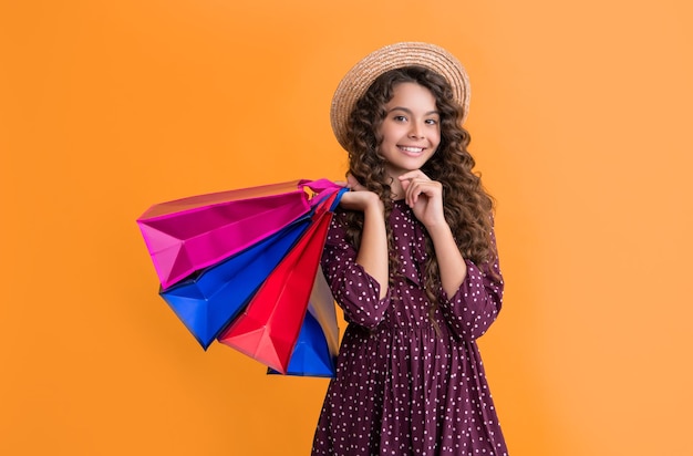 criança feliz com cabelos encaracolados segurar sacos de compras em fundo amarelo