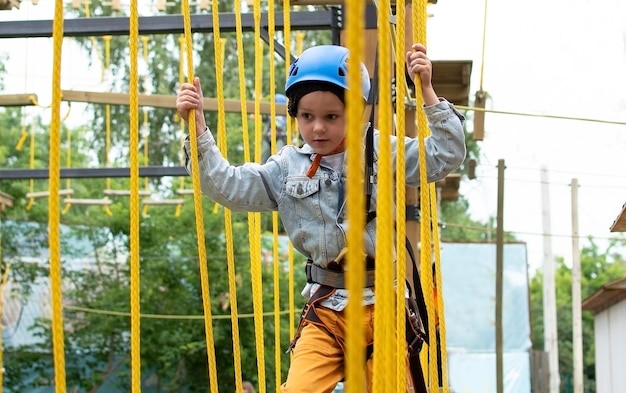 Criança feliz com capacete e equipamento de proteção gosta de aulas em um parque de aventura de escalada em um dia de verão