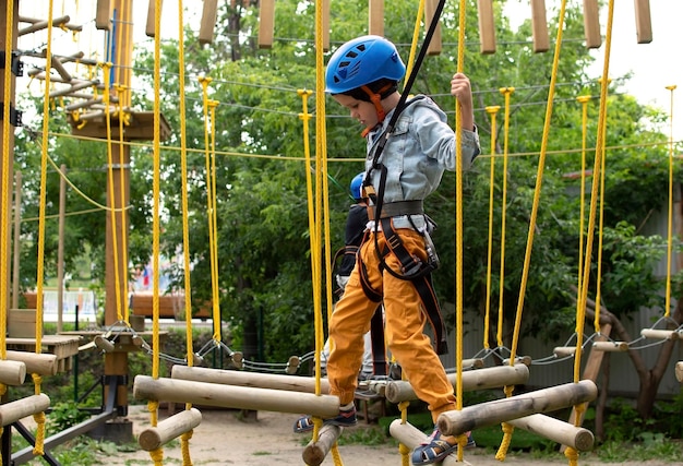 Criança feliz com capacete e equipamento de proteção gosta de aulas em um parque de aventura de escalada em um dia de verão