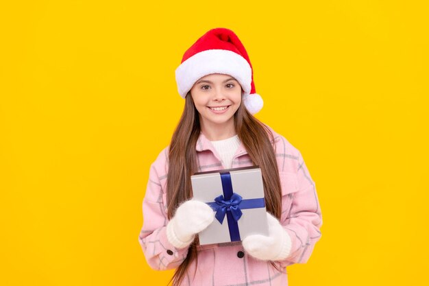 Criança feliz com chapéu de papai noel e luvas seguram caixa de presente no natal de fundo amarelo